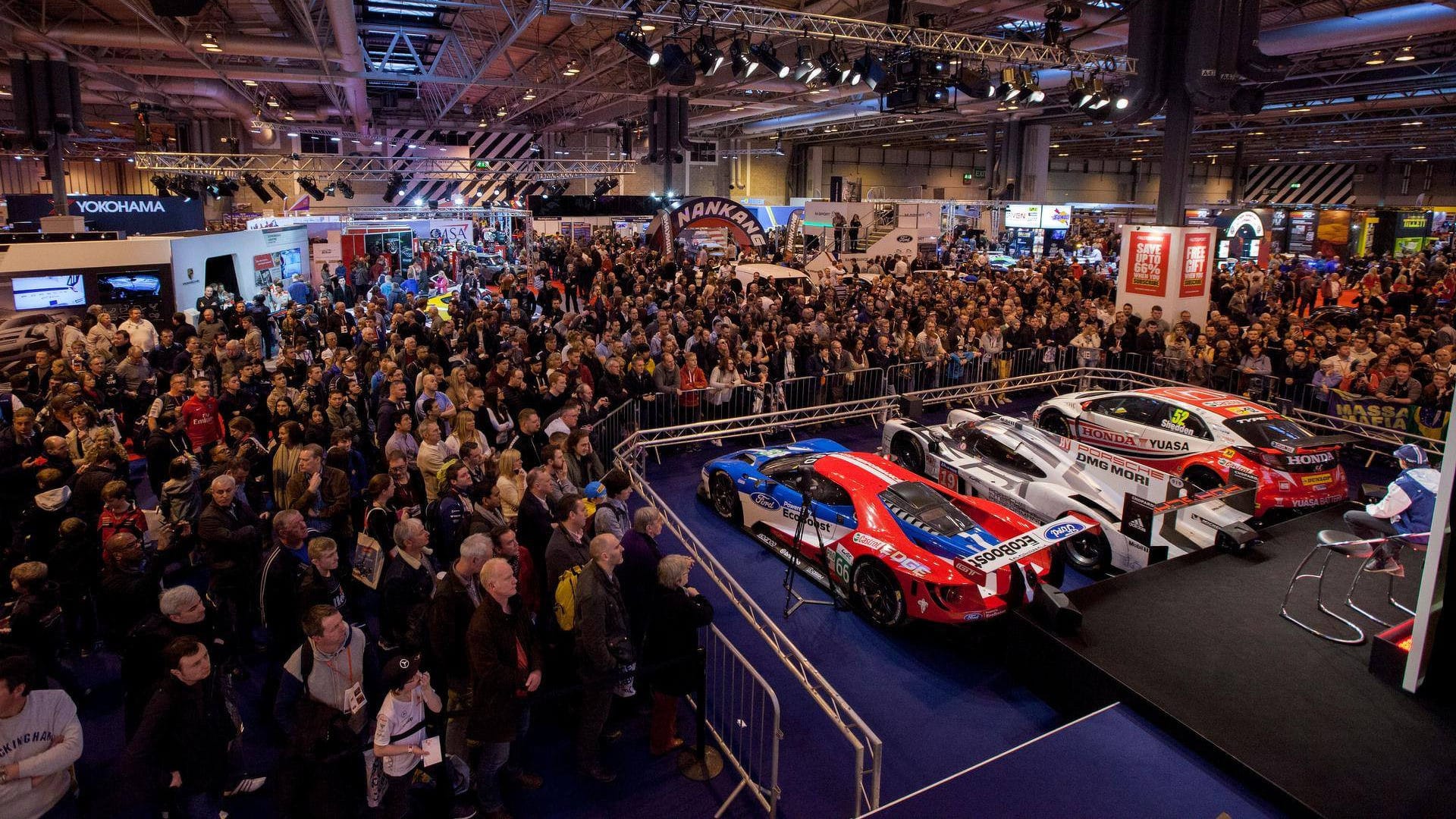 Busy exhibition hall at Autosport International with crowds of visitors and race cars on display