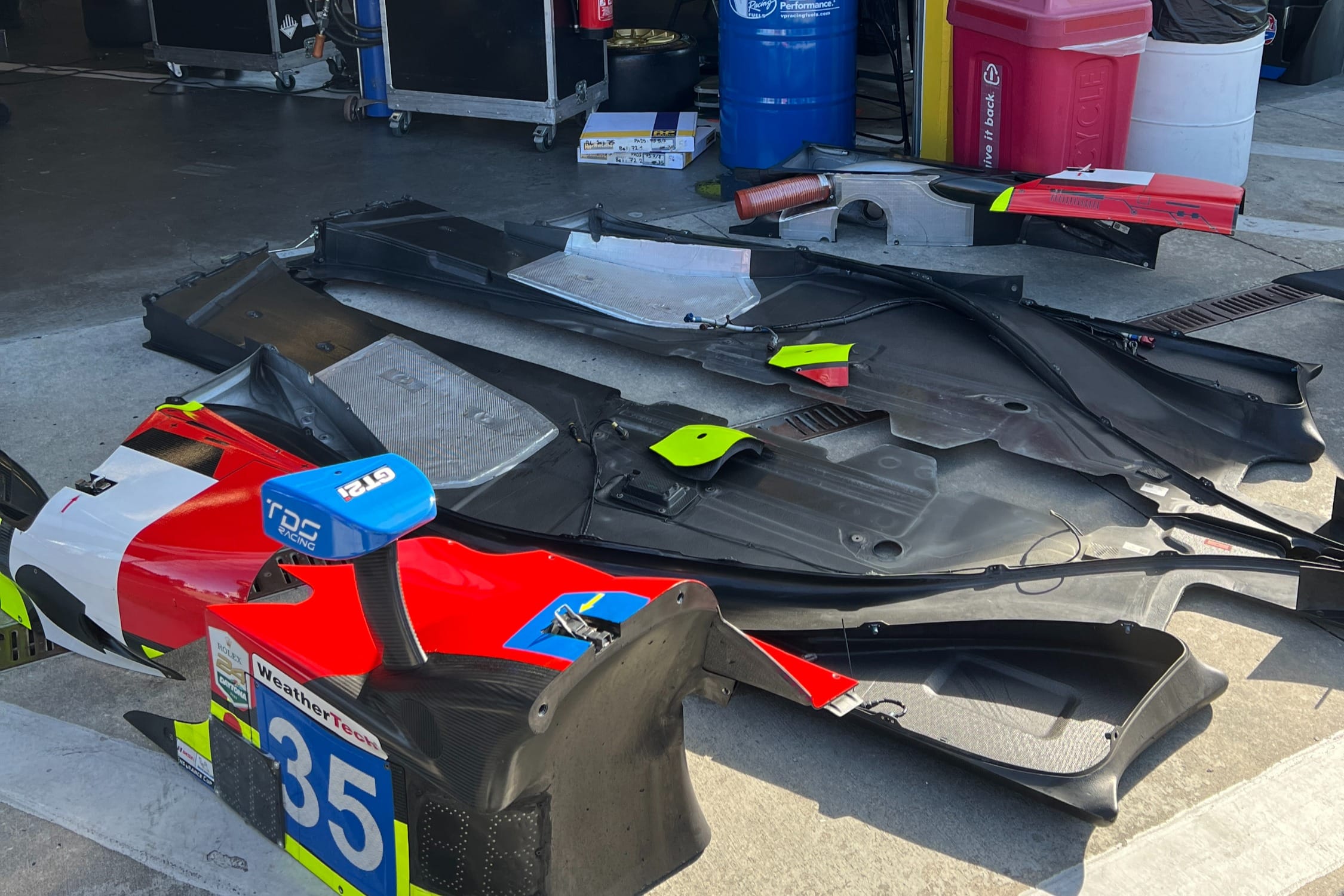 LMP2 prototype car in the garage at Daytona with bodywork removed, aerodynamic panels laid out on the floor