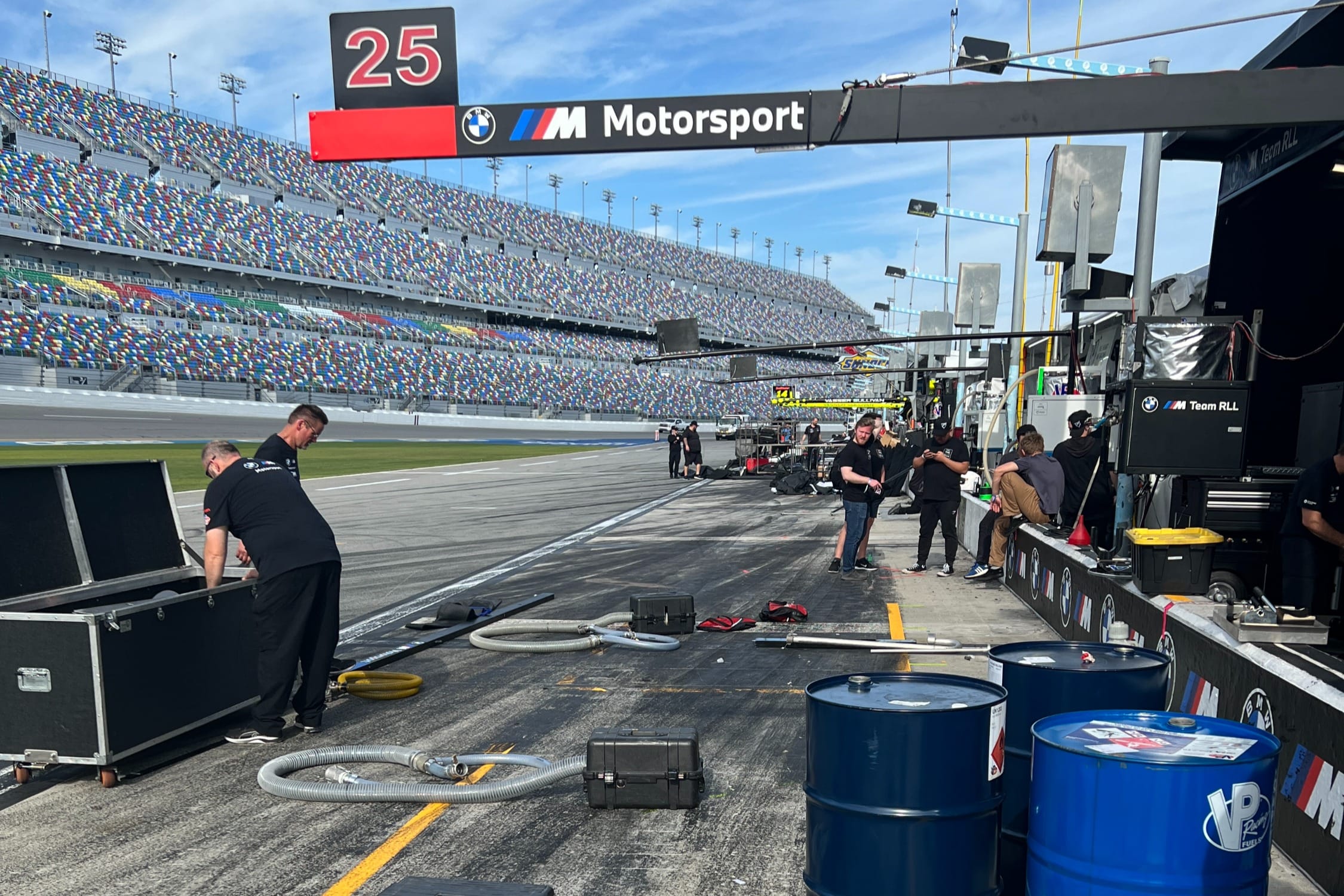 BMW M Motorsport pit lane at Daytona during pre-race preparations, with packed grandstands visible in the background