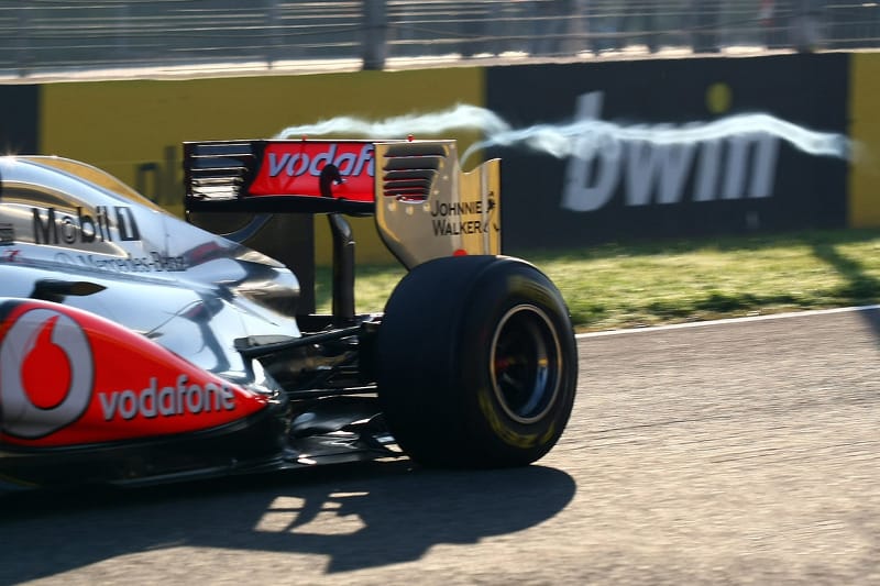 McLaren F1 car with visible condensation vortex trailing from the rear wing tip, demonstrating aerodynamic vortex formation