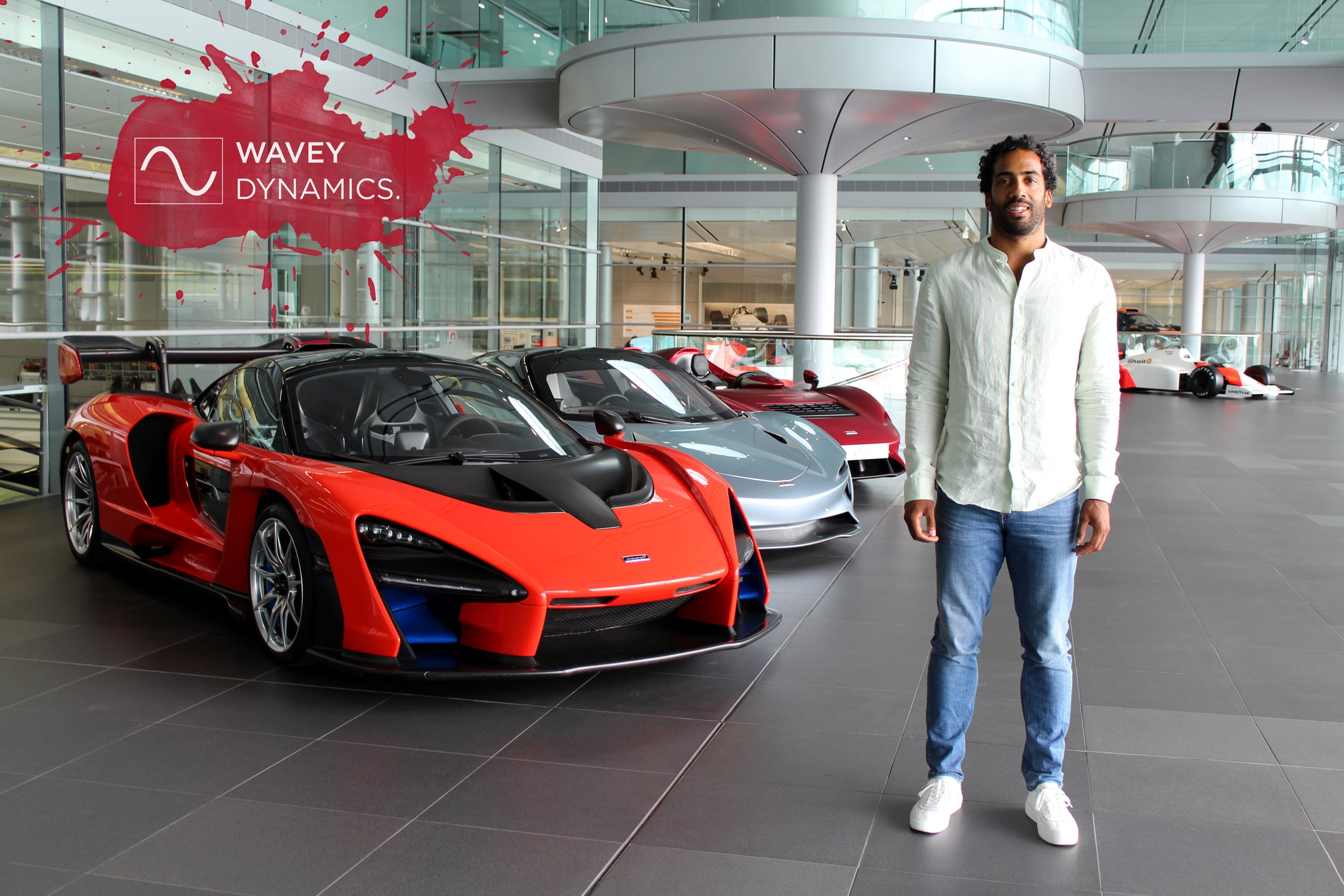 Wavey Dynamics director Jahee Campbell-Brennan standing in the McLaren Technology Centre showroom alongside a red McLaren Senna supercar