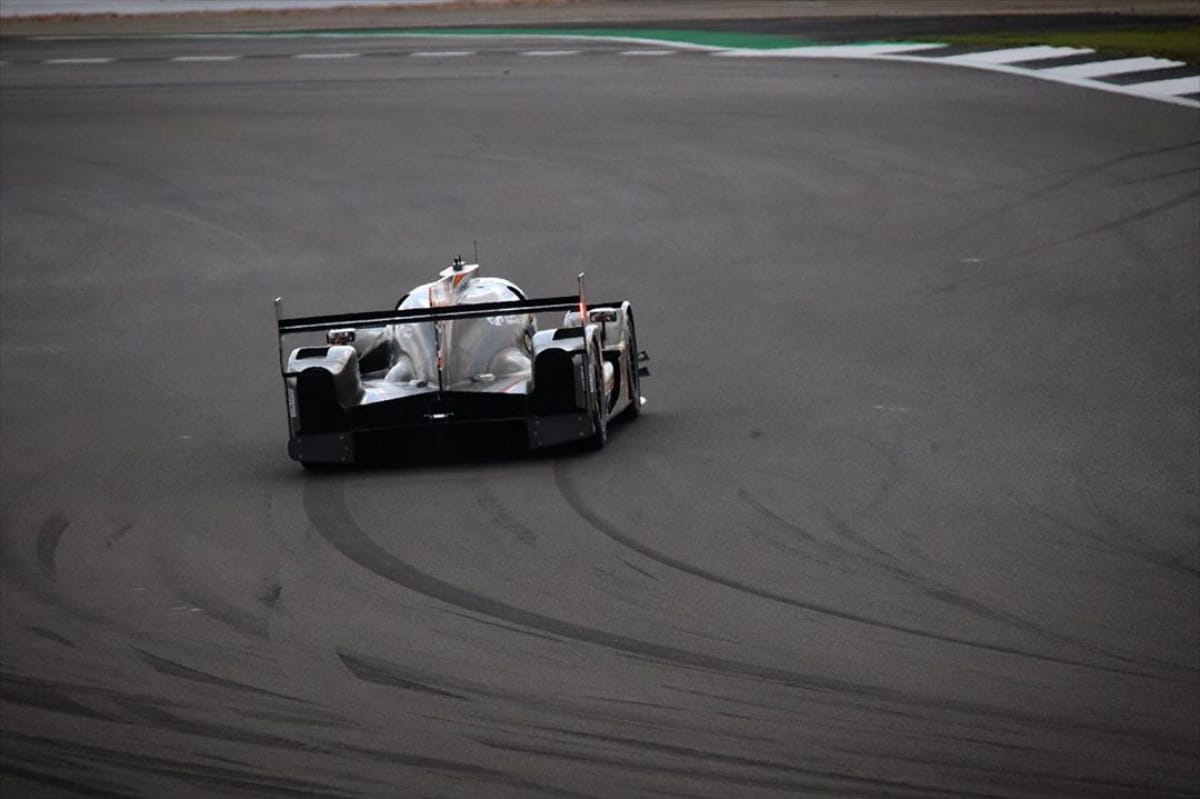 LMP racing car cornering at speed, showing body roll with tyre skid marks from lateral weight transfer visible on track
